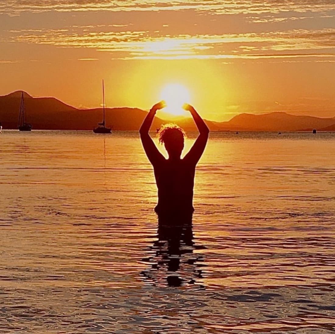 Sunrise in the water, arms cradling the sun — the Rise & Shine retreat